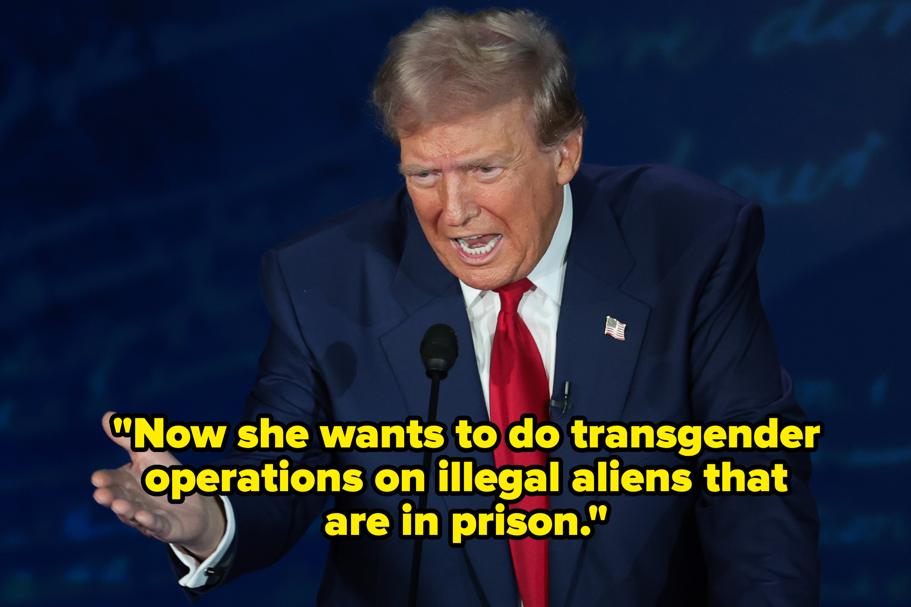 Donald Trump speaking at an event, wearing a dark suit, white shirt, and red tie. He is gesturing with his right hand
