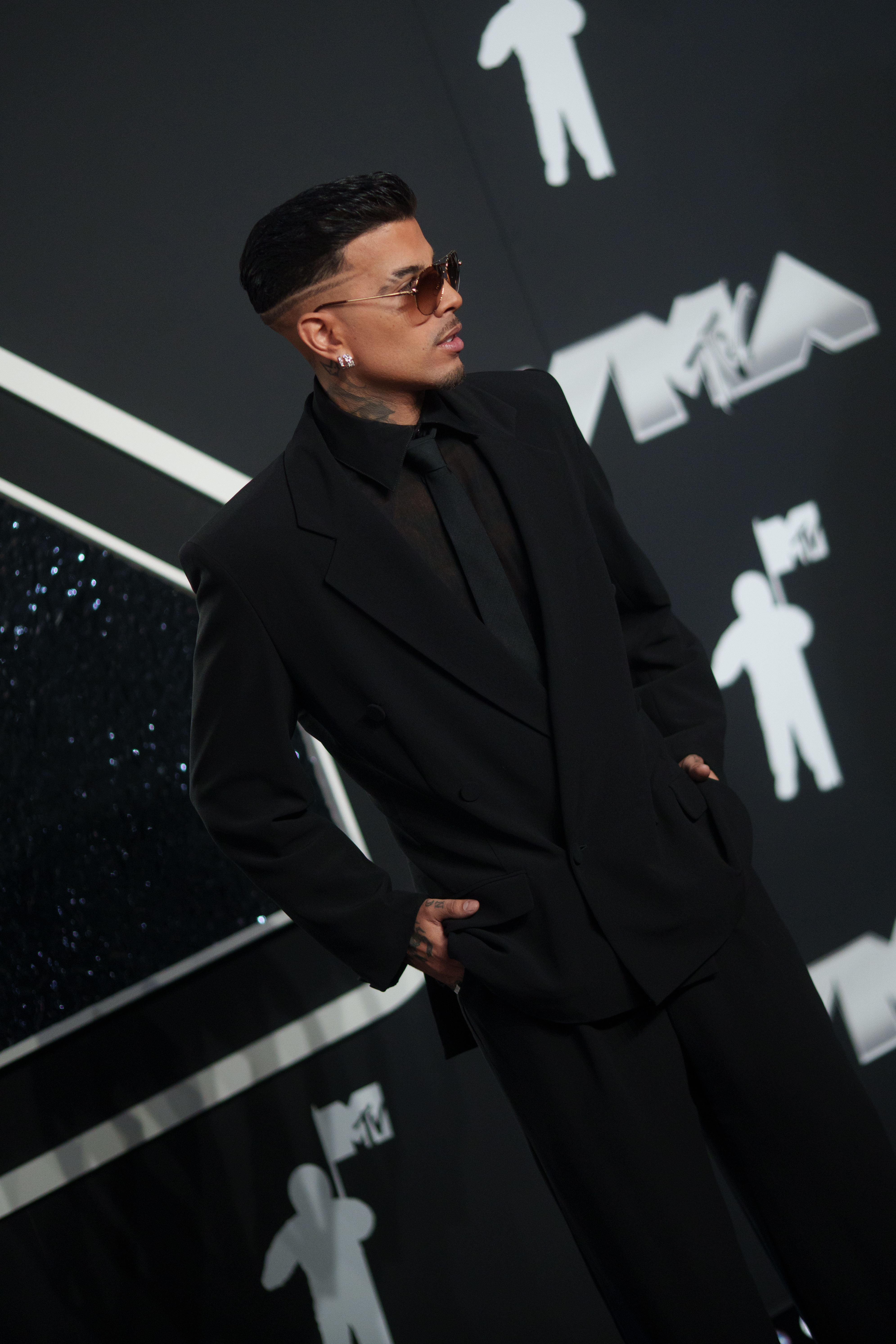 Un hombre con gafas de sol y traje negro de corte elegante en la alfombra roja de los premios MTV