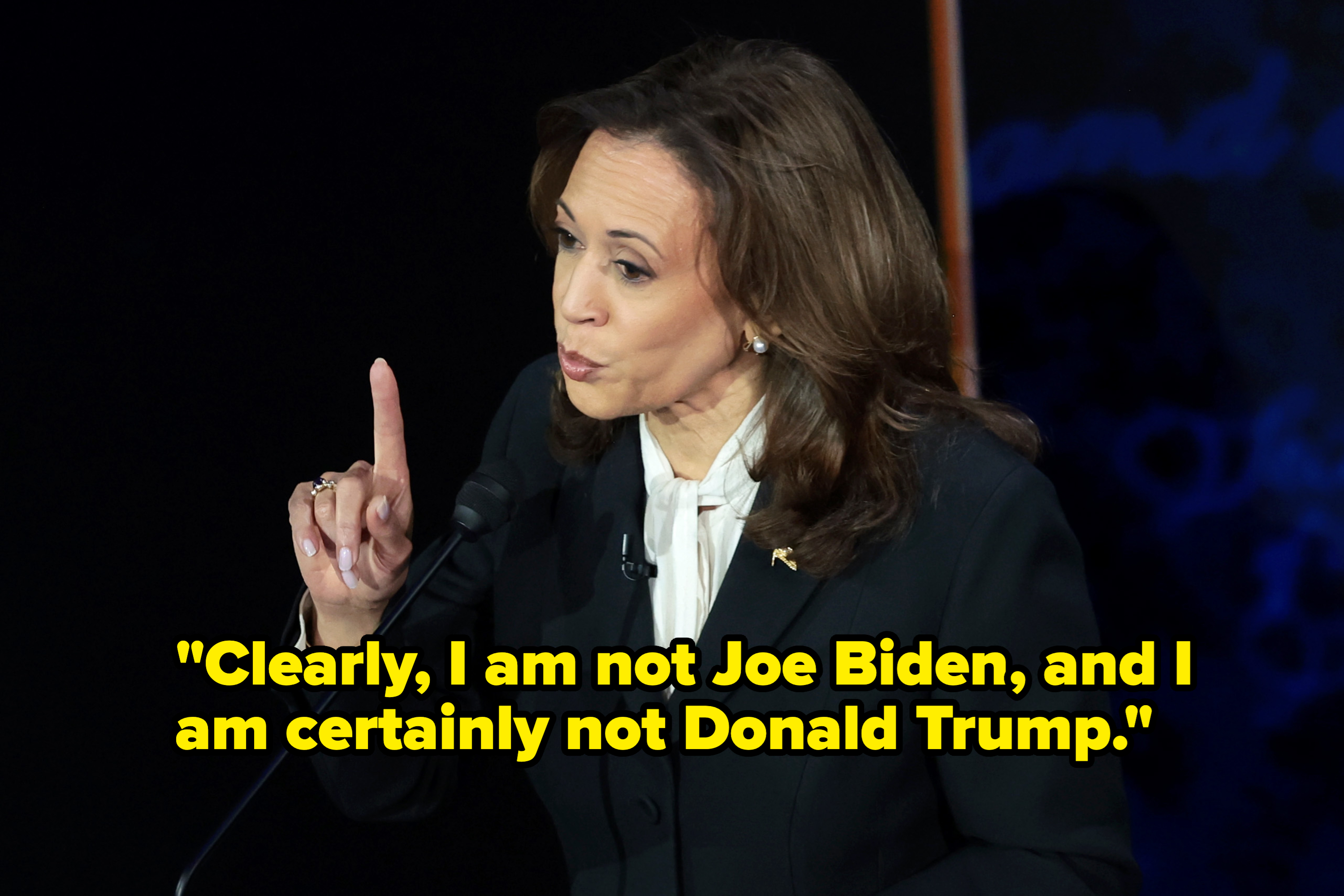 Kamala Harris gestures while speaking at a podium, wearing a dark suit with a light-colored blouse