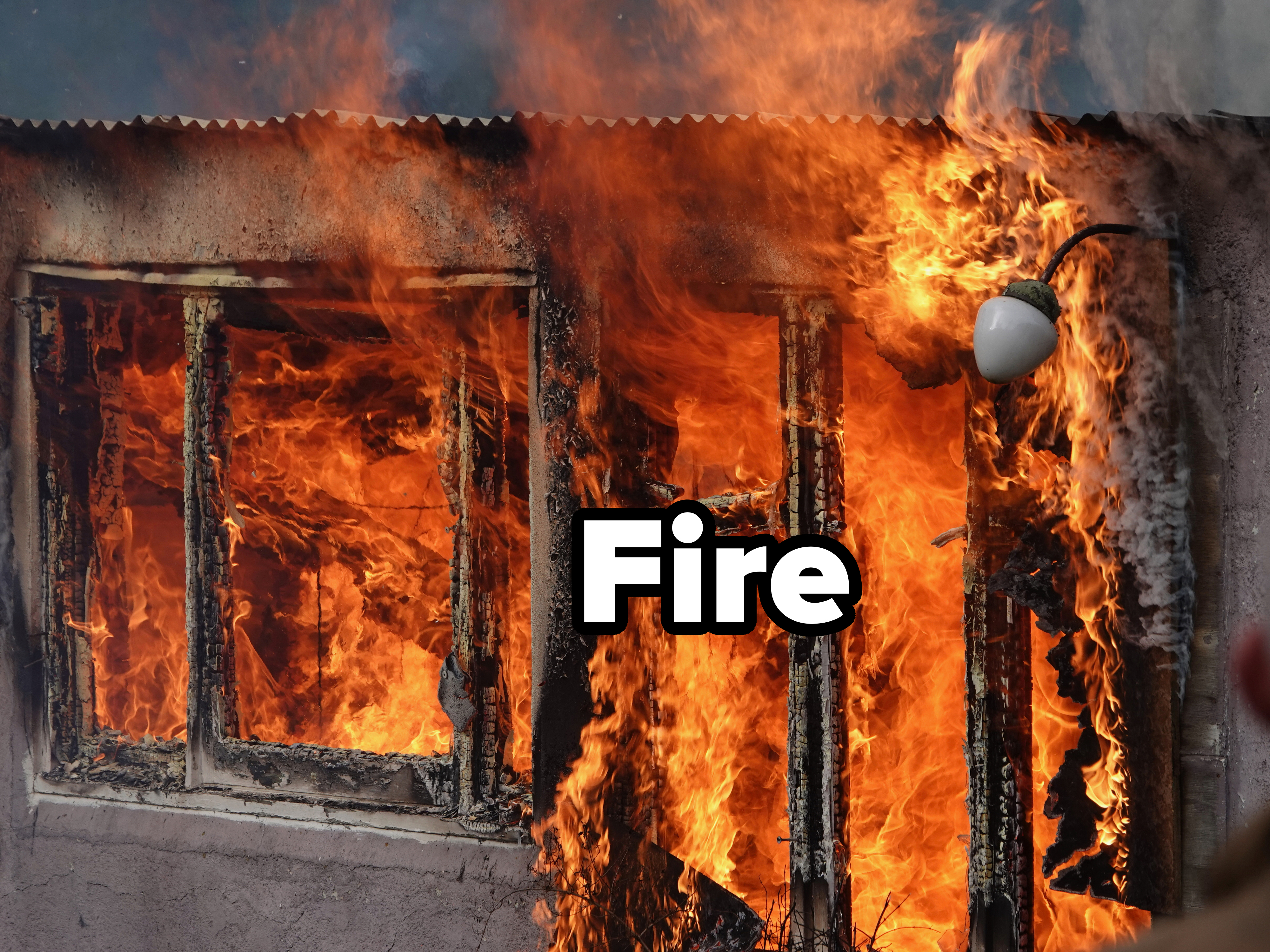 A building with wooden window frames is engulfed in flames