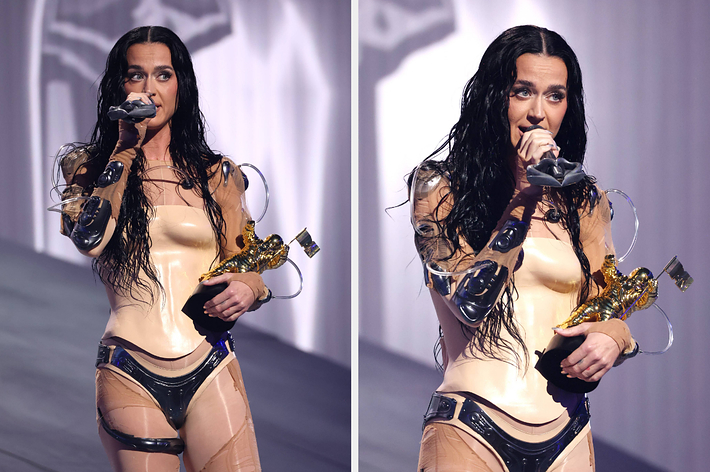 Katy Perry on stage in a futuristic outfit, holding a gold award and speaking into a microphone