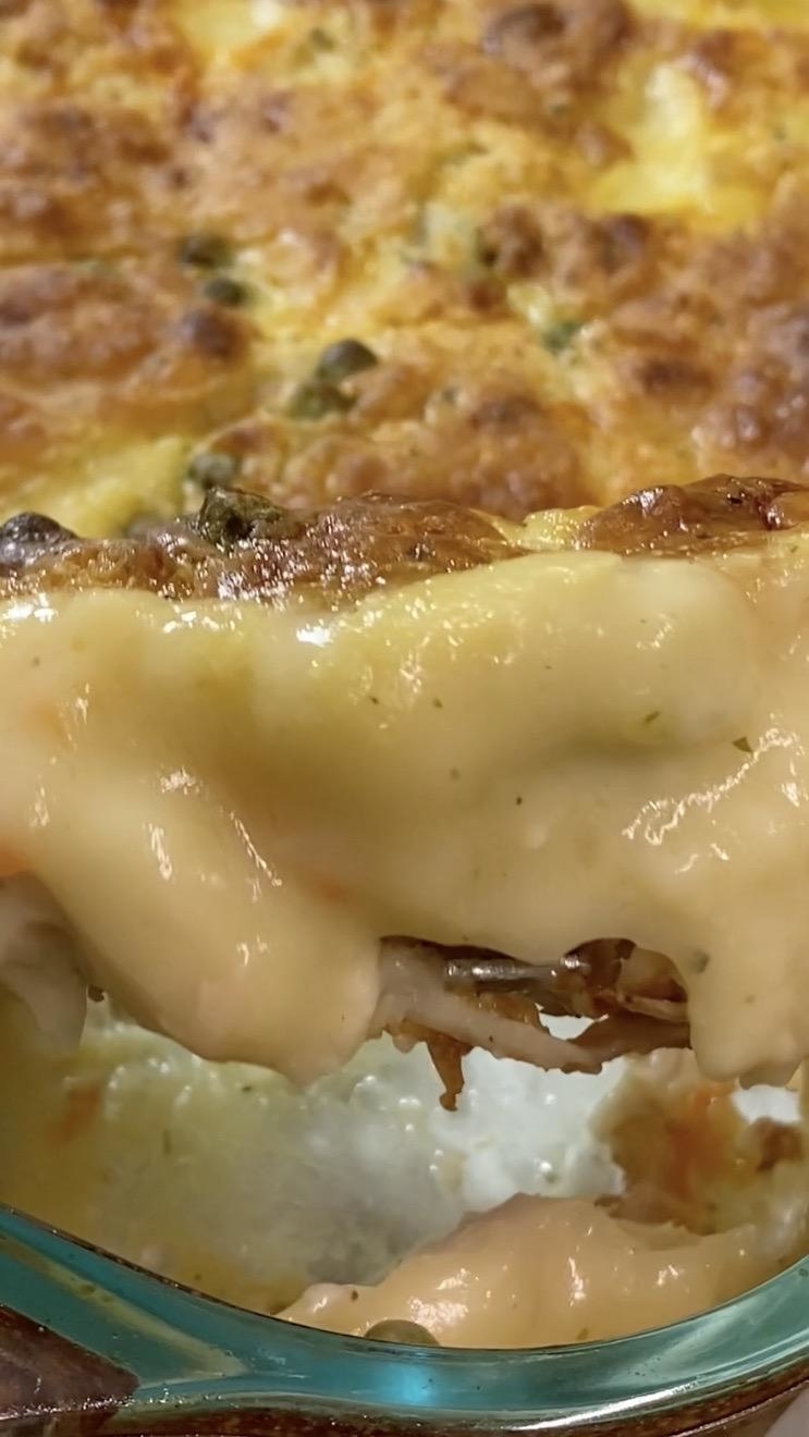 A slice of creamy, cheesy lasagna being lifted from a glass baking dish, with a golden, bubbly top and visible layers of melted cheese and sauce