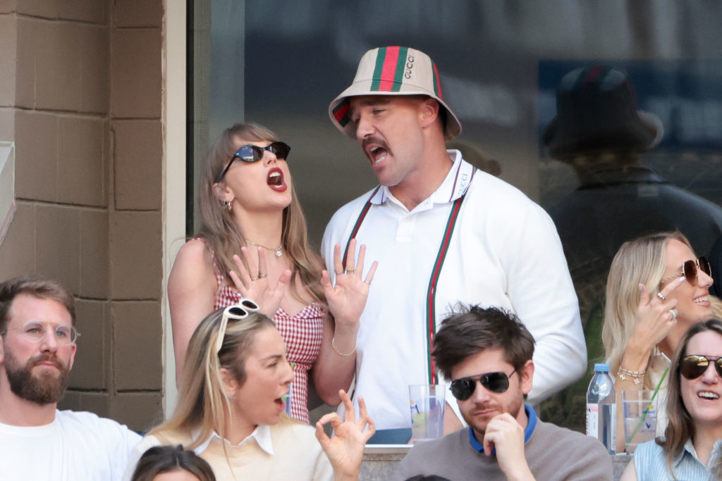 Taylor Swift and Travis Kelce at a public event; both appear excited, with their mouths open wide while gesturing with their hands