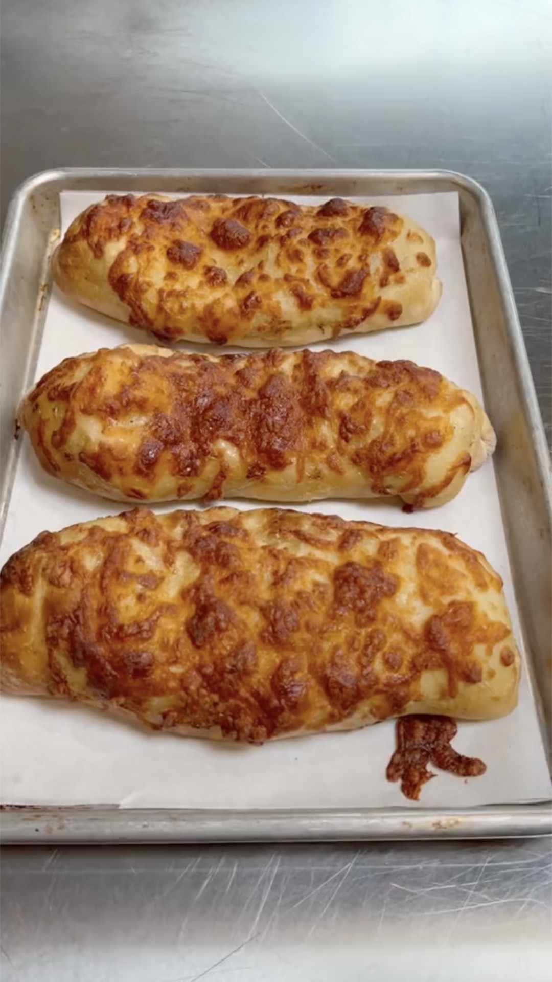 Three freshly baked cheese-covered breadsticks on a baking sheet