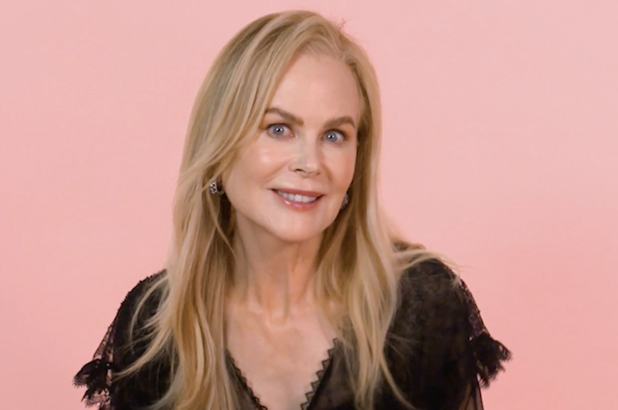 Nicole Kidman is posing and smiling, wearing a lace dress with sheer sleeves