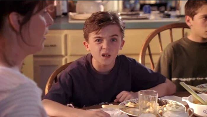 Frankie Muniz sitting at a table looking confused, with a woman on the left partially shown and another person in the background