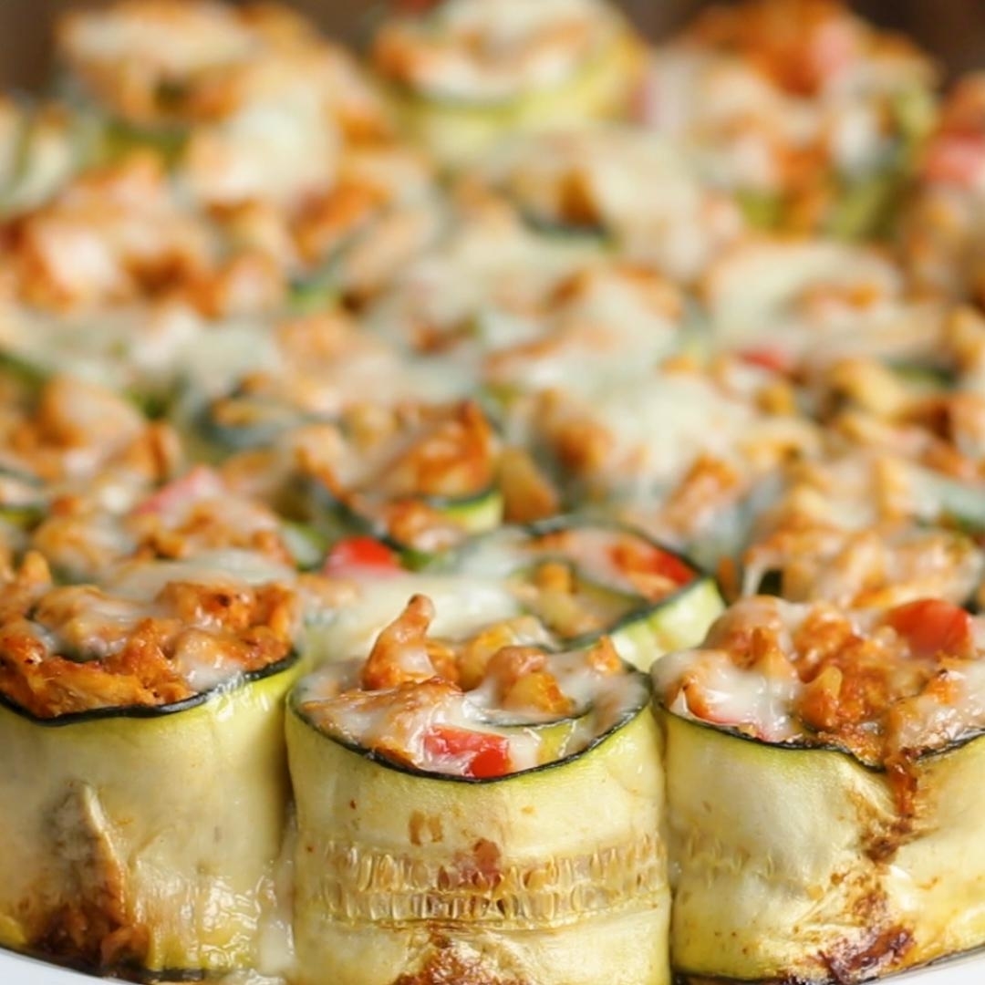 Close-up of zucchini rolls stuffed with chicken, tomatoes, and topped with melted cheese. The dish appears freshly baked and ready to eat