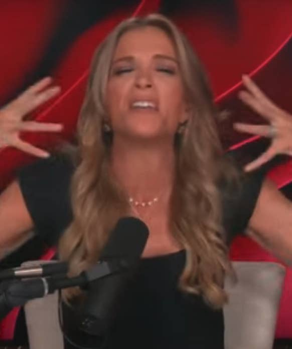 Woman on a podcast, wearing a black top and gesturing expressively near a microphone with a vibrant, patterned background