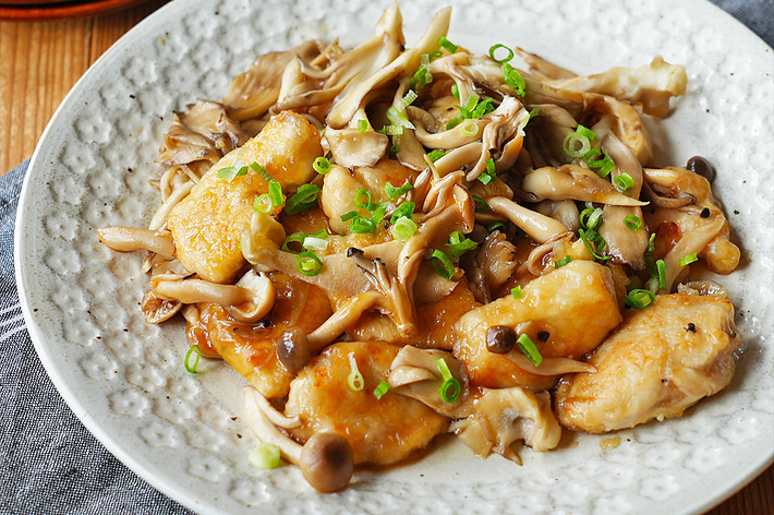 皿に盛り付けられた鶏肉ときのこの炒め物。上に小ねぎが散らしてある。手前には箸が乗った器が見える。