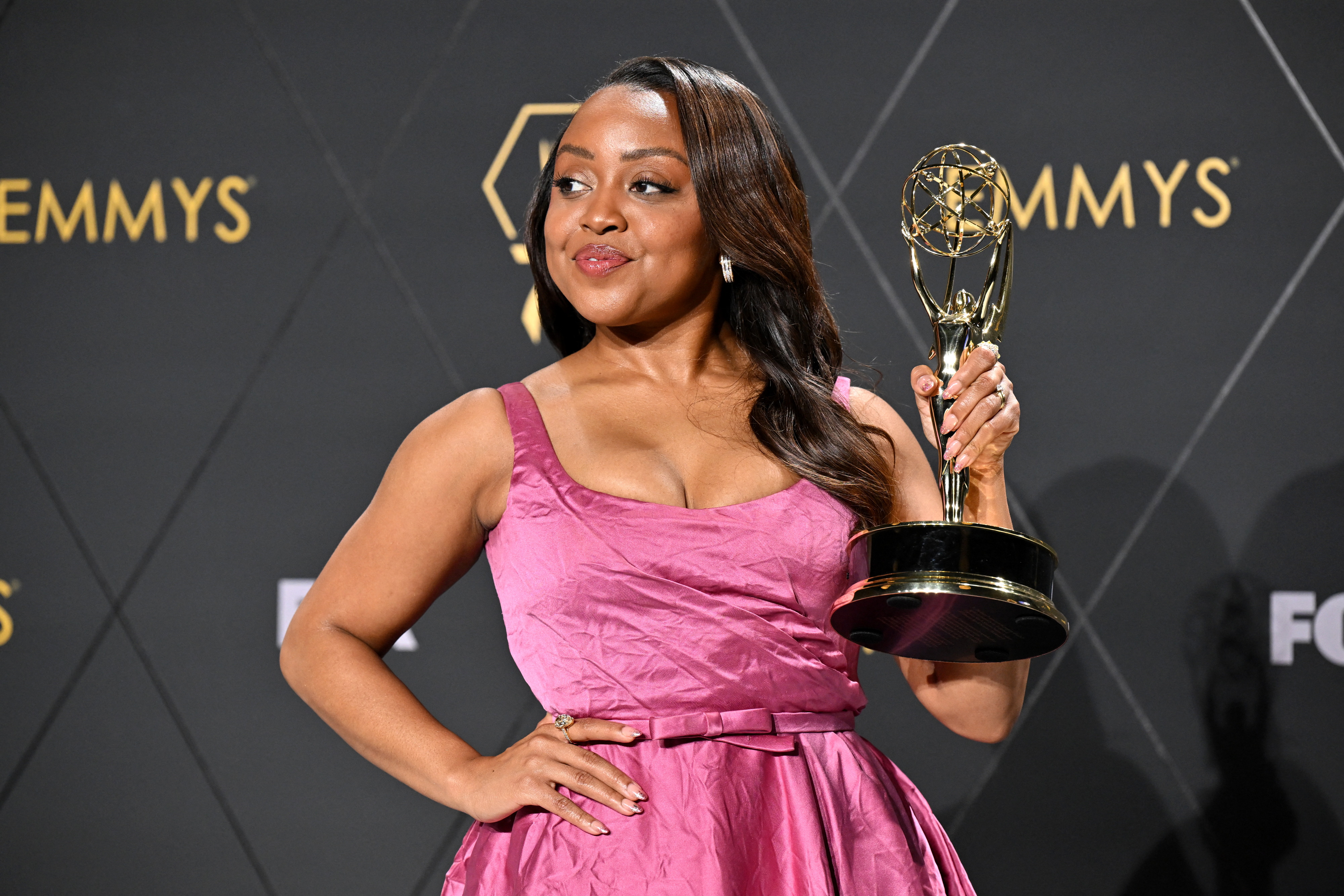Quinta Brunson poses with her Emmy award, dressed in a sleeveless, elegant gown, against an Emmy Awards backdrop