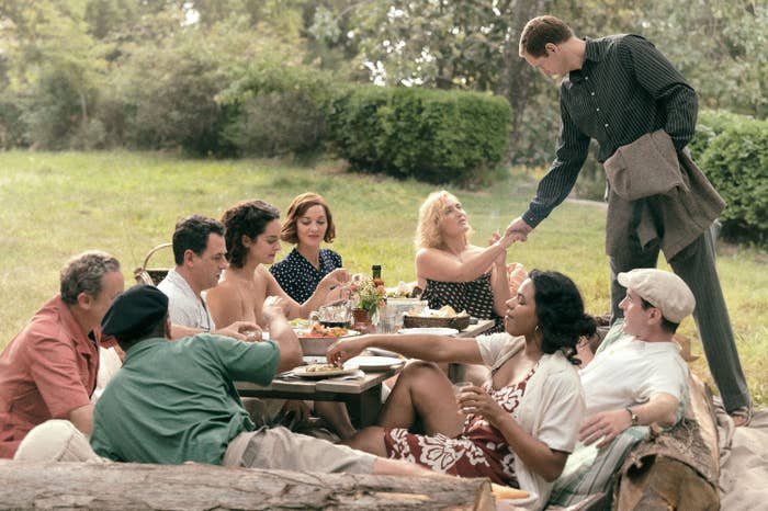 Group of people having a picnic, two individuals shaking hands on the right. This scene includes individuals dining and chatting outdoors