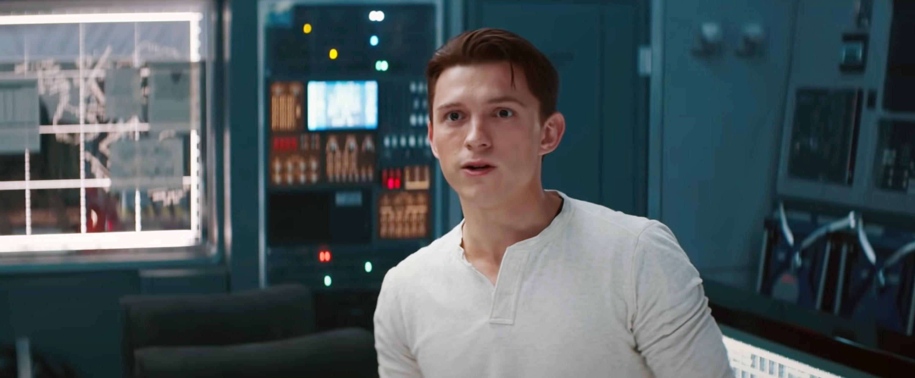 Tom Holland in a scene from a movie, standing in a futuristic control room with various monitors and equipment
