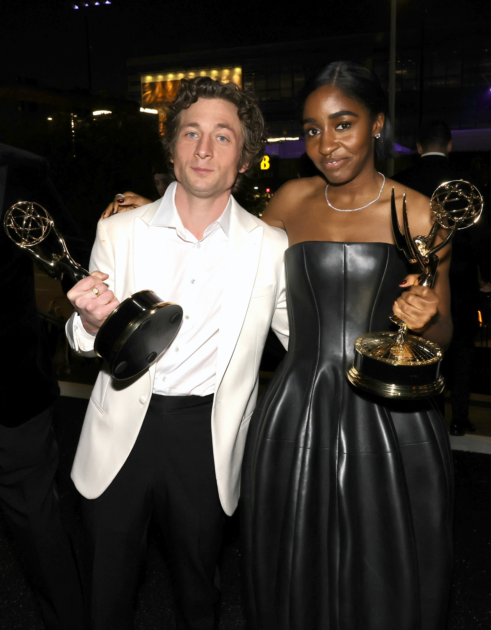 Jeremy Allen White in a white suit jacket and Ayo Edebiri in a strapless black dress hold their Emmy awards