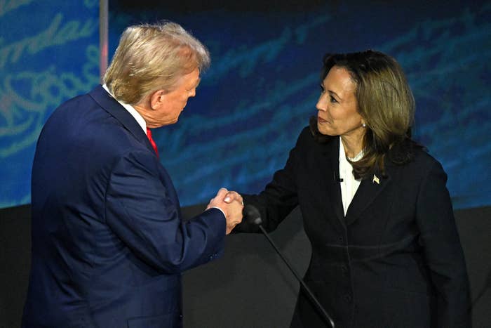 Donald Trump and Kamala Harris in formal attire shaking hands on stage at a public event