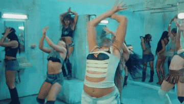 Group of dancers performing energetically in a room, all wearing stylish, revealing outfits with various cut-out designs