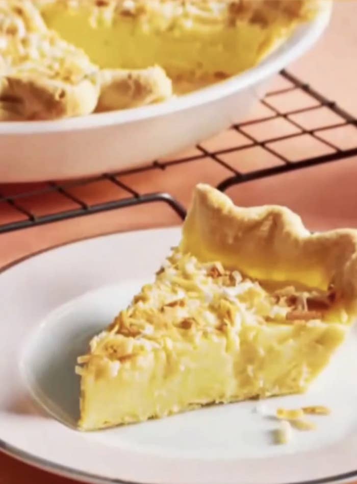 A slice of pie with a flaky crust and creamy filling on a plate, with the whole pie in the background