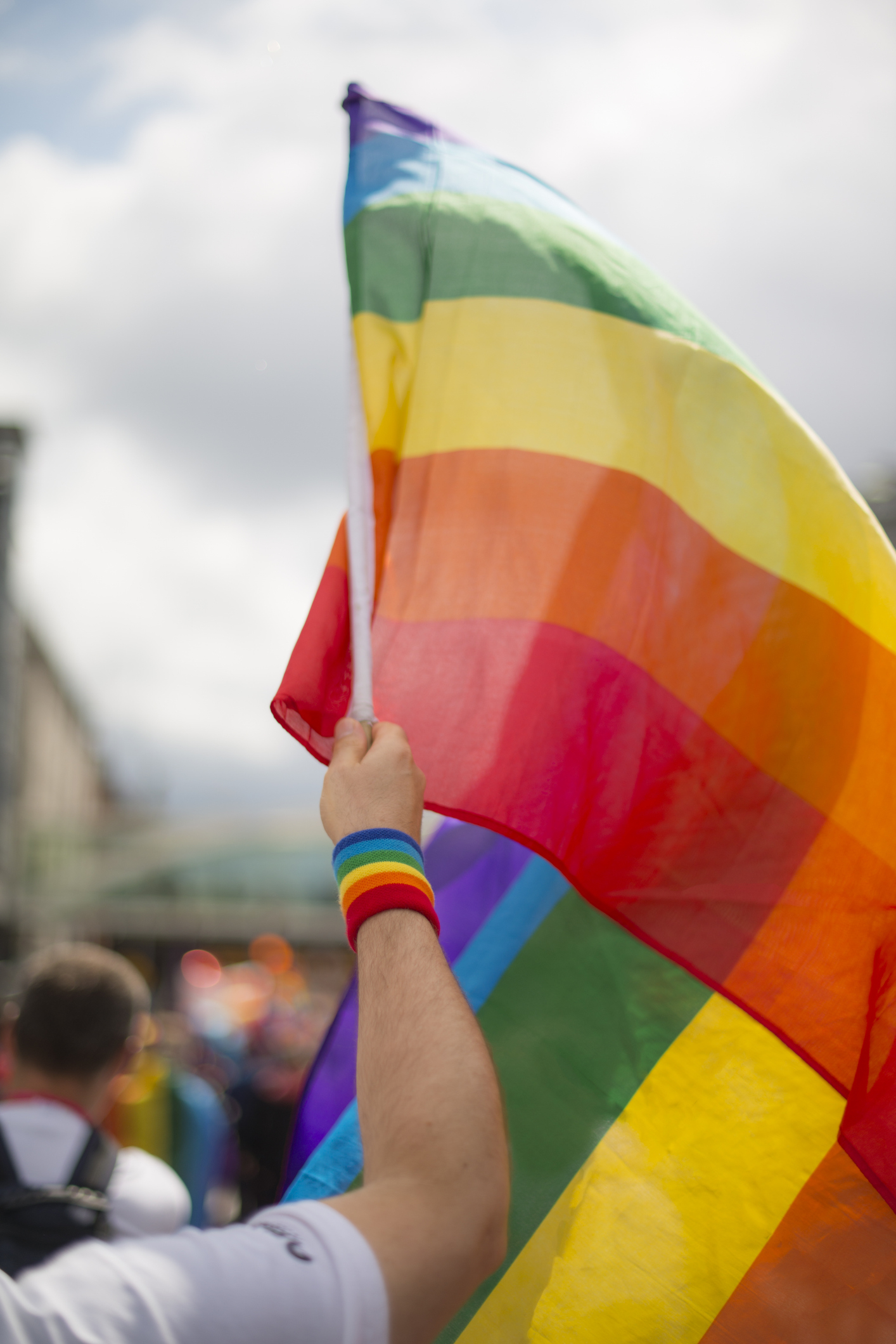 A person holding a rainbow flag at a parade, wearing a rainbow wristband