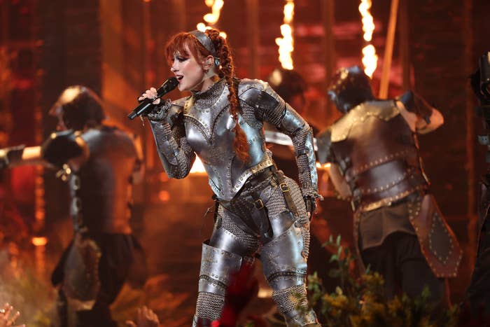 Chappell Roan performs in an elaborate knight costume with metallic armor on stage, surrounded by dancers in similar medieval outfits