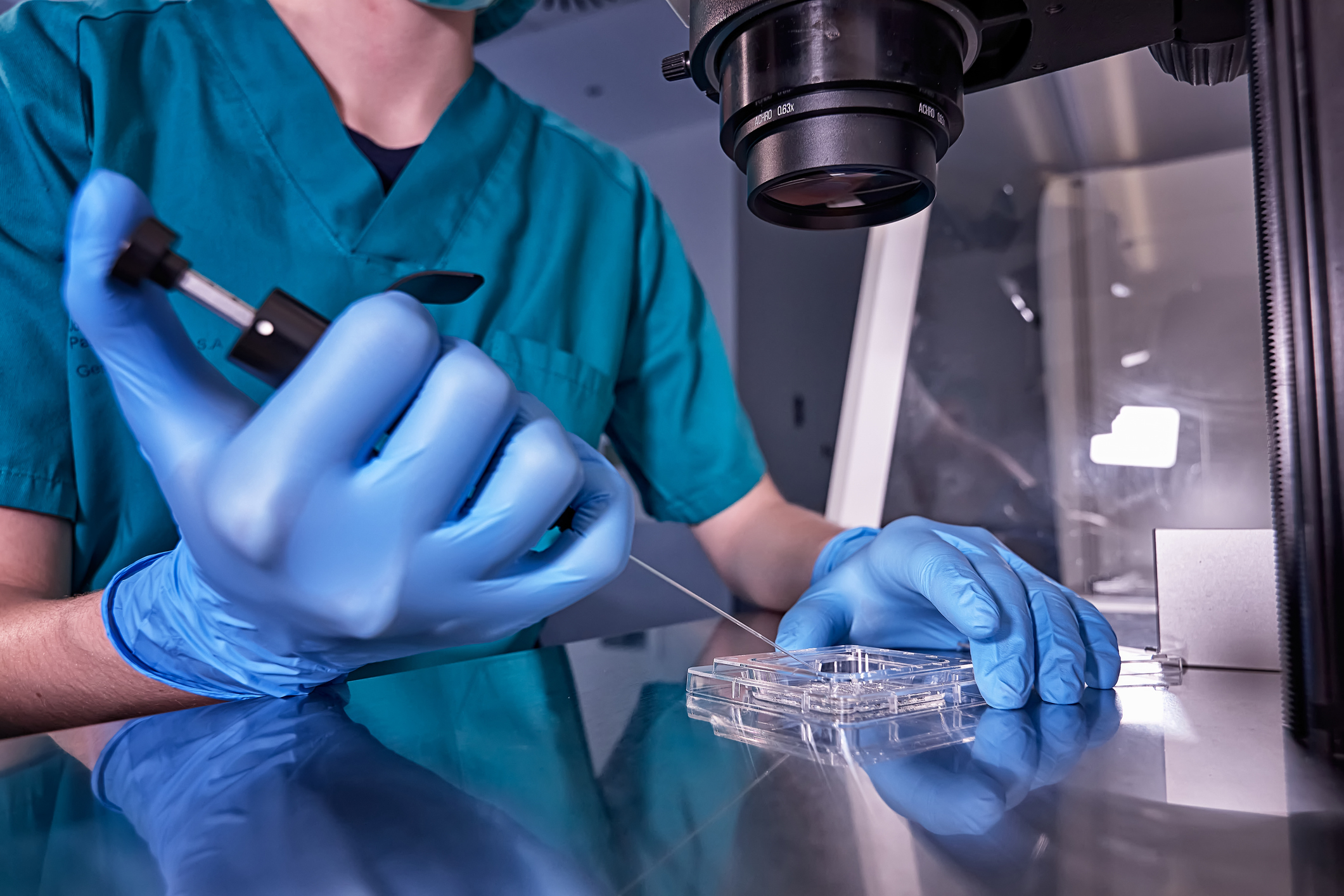 A scientist in lab attire uses a pipette to carefully handle samples under a microscope in a laboratory setting