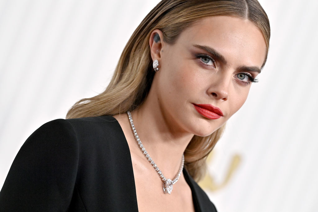 Cara Delevingne poses in a sophisticated black outfit with a plunging neckline, accessorized with diamond jewelry
