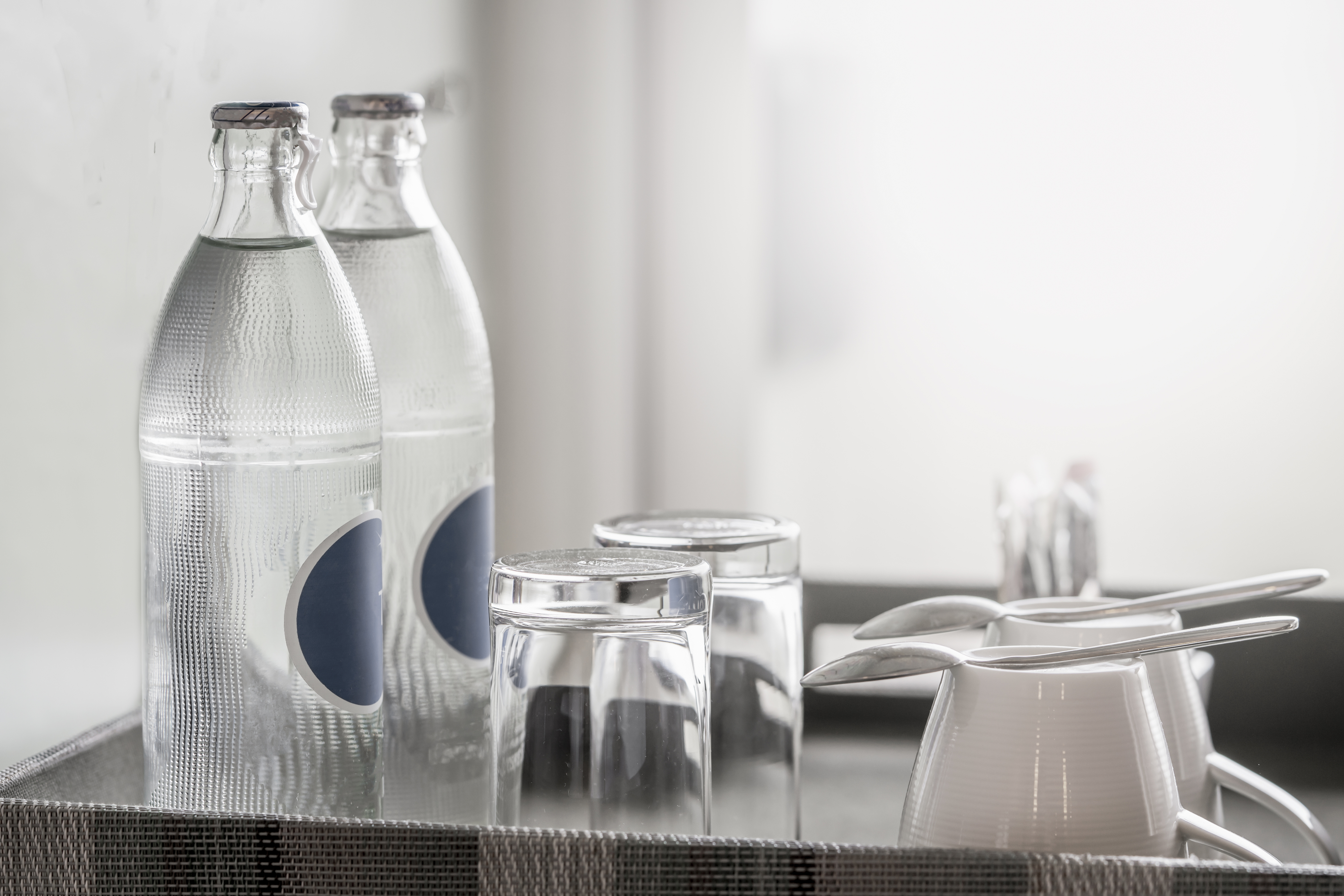 Two water bottles, four glasses, a creamer, and spoons arranged on a tray in a well-lit setting