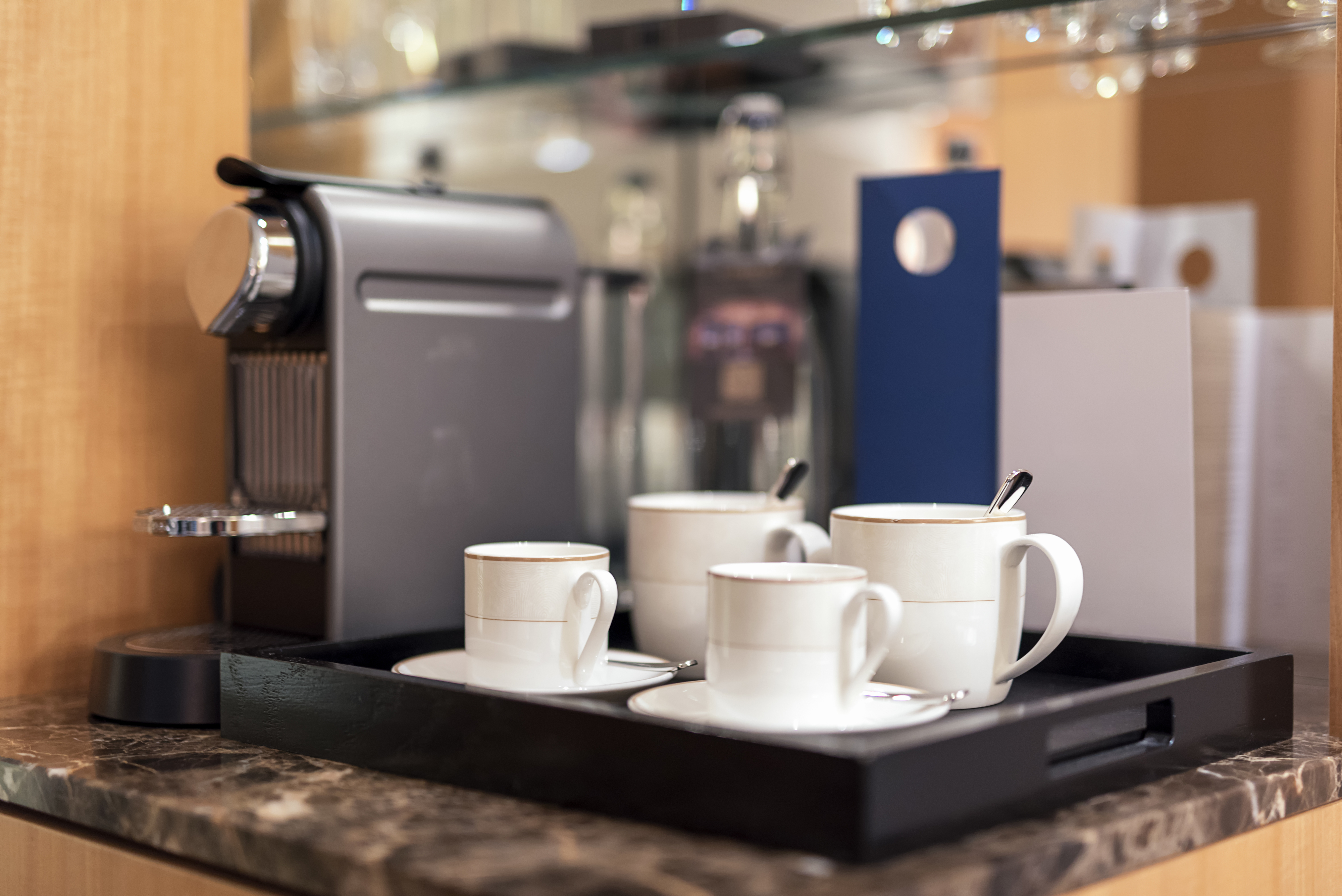 Coffee machine on a counter with four white coffee mugs on a tray, each mug with a spoon