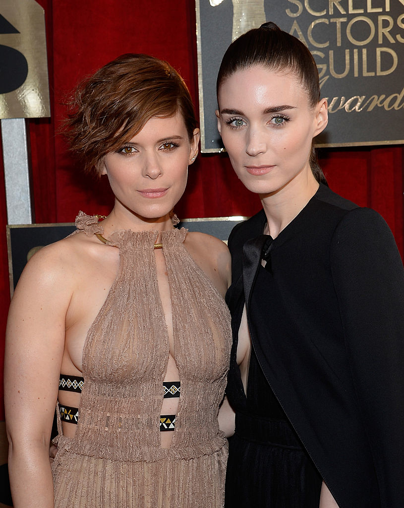 Kate Mara and Rooney Mara on the red carpet; Kate wears a sleeveless gown with intricate details, while Rooney is in a black dress with a high neckline and cape