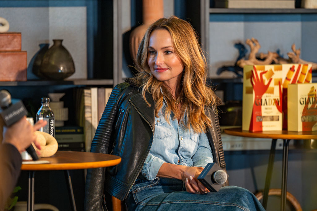 Giada De Laurentiis sits onstage wearing a denim outfit and leather jacket, holding a microphone during an interview. A person with a microphone faces her