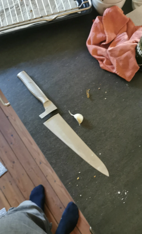 A kitchen knife lies on a dark countertop next to a clove of garlic and a cloth