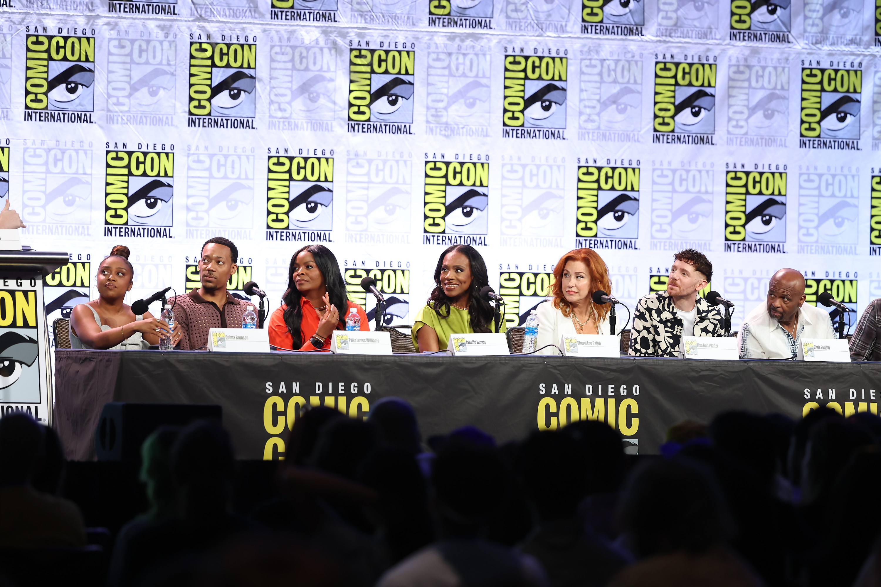A panel of speakers at San Diego Comic-Con, discussing in front of an audience. Comic-Con banners are in the background