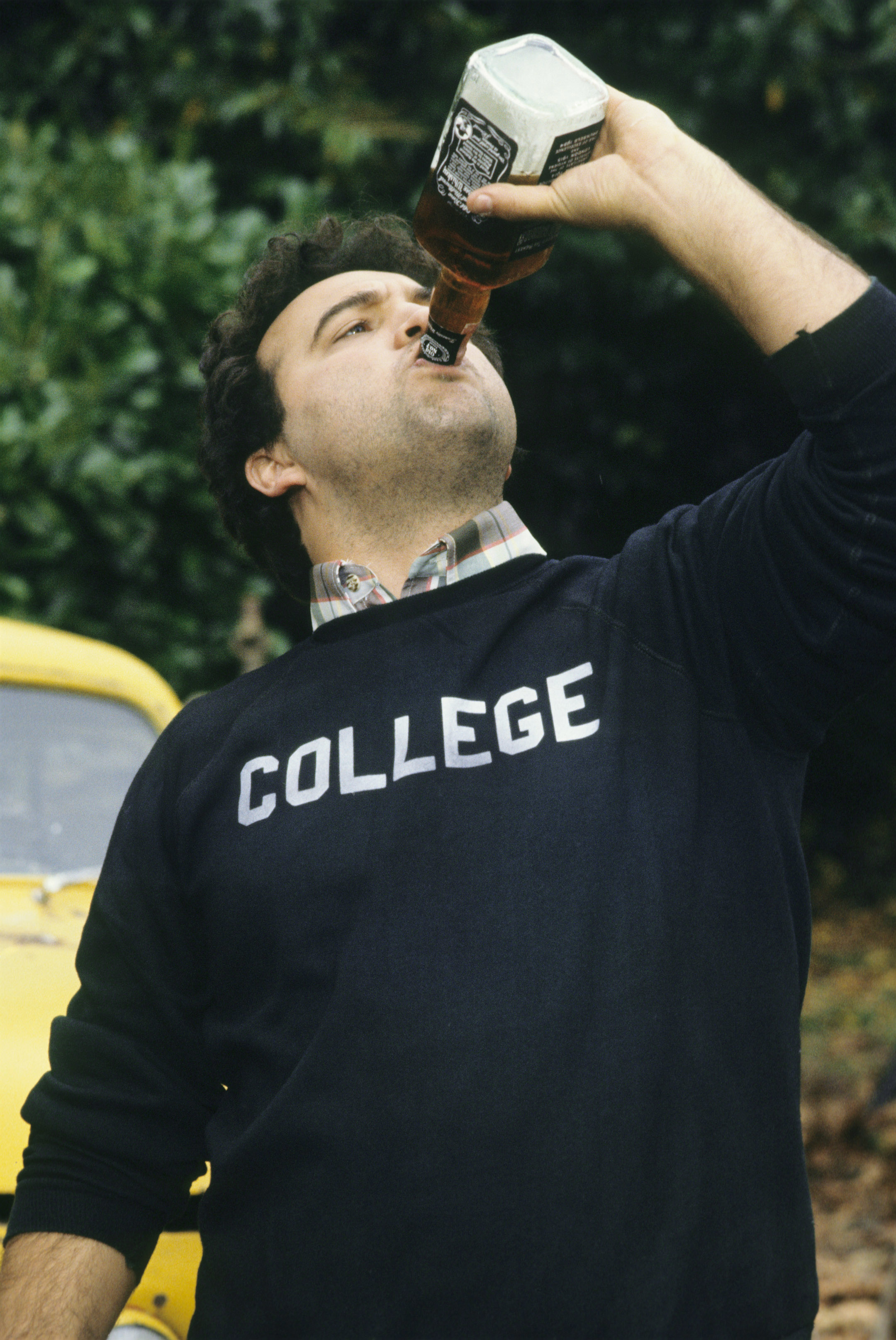 John Belushi in a "College" sweatshirt drinks from a bottle in a scene from the movie Animal House