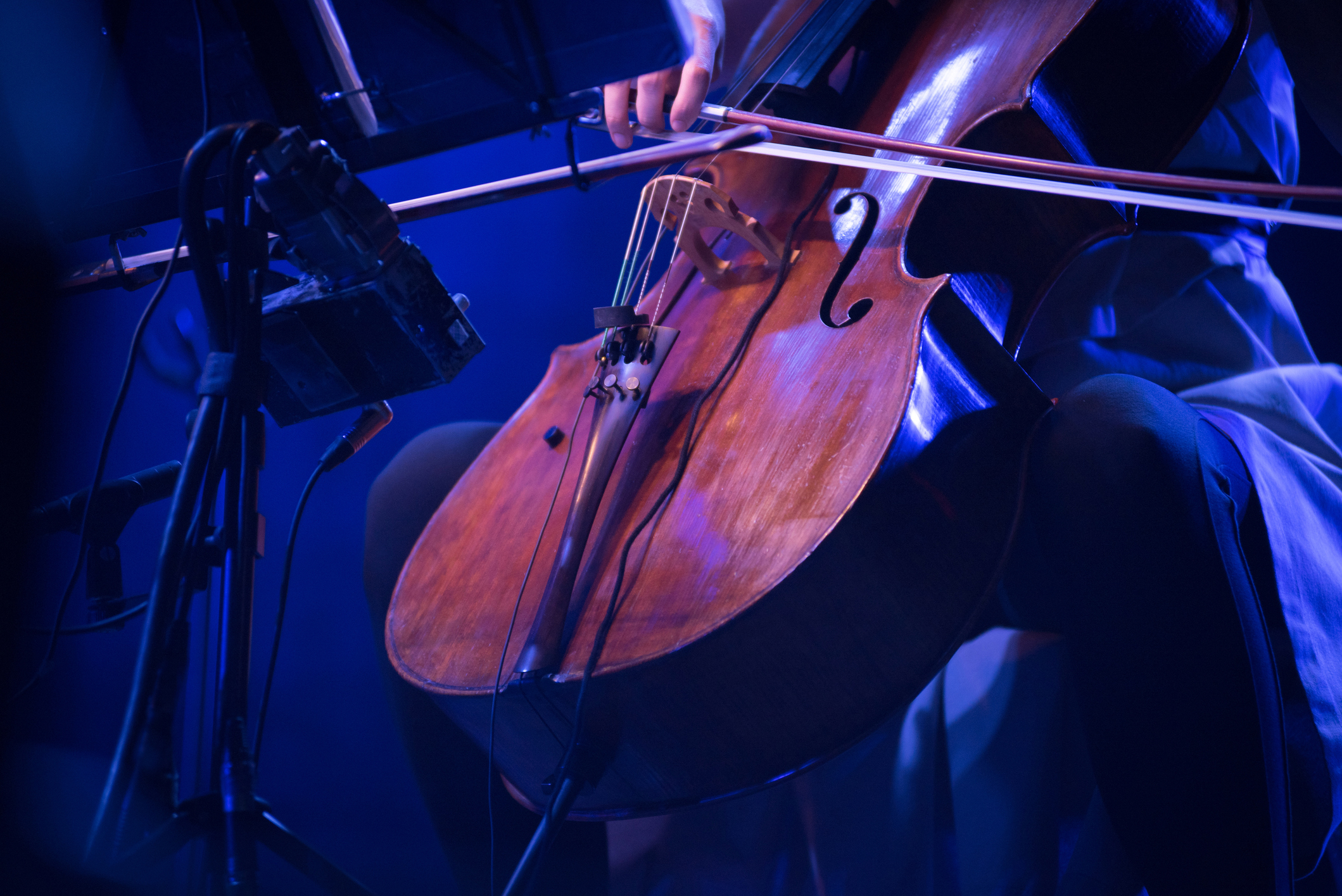 A close-up of a musician playing a cello, focusing on the instrument and bow in action. The musician's face is not visible
