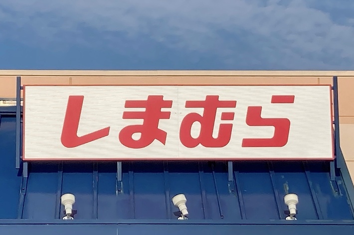 Storefront sign in Japanese script reading &ldquo;Shimamura&rdquo; over the entrance of a retail store with an accessible parking sign visible in the foreground