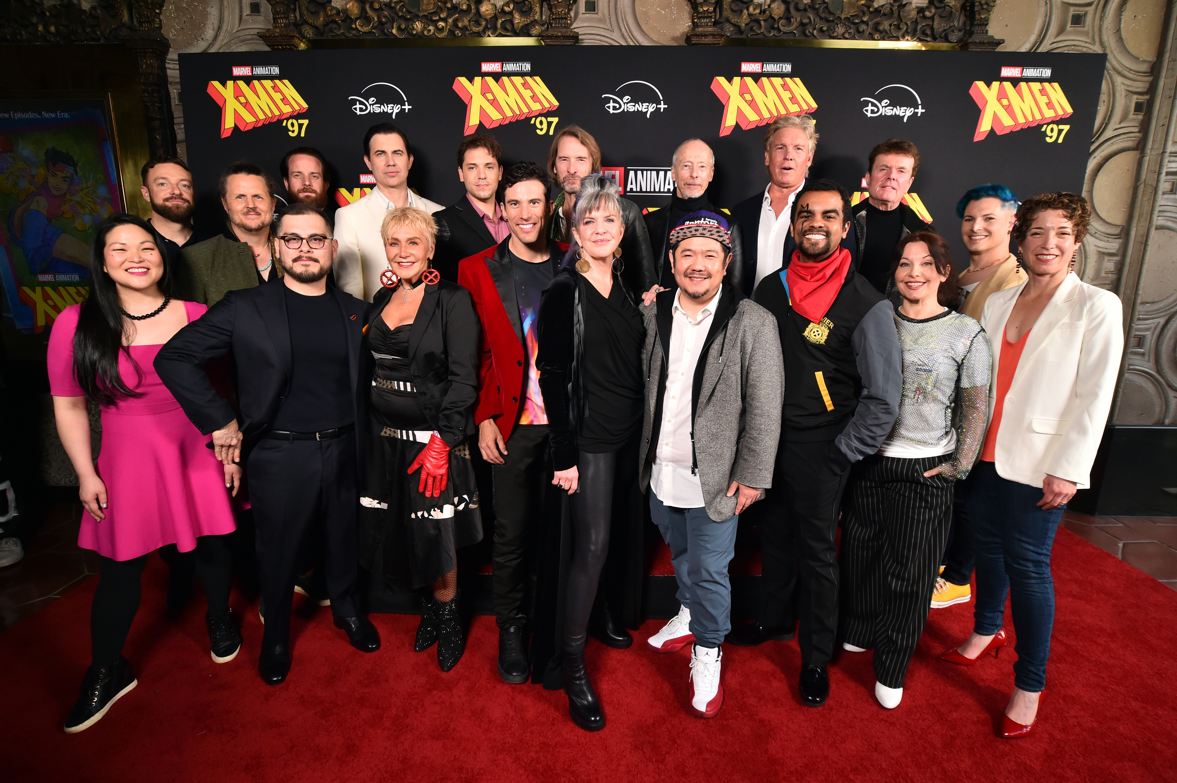 The cast and crew of "X-Men '97" stand together on a red carpet, smiling. They are dressed in a variety of styles from casual to formal