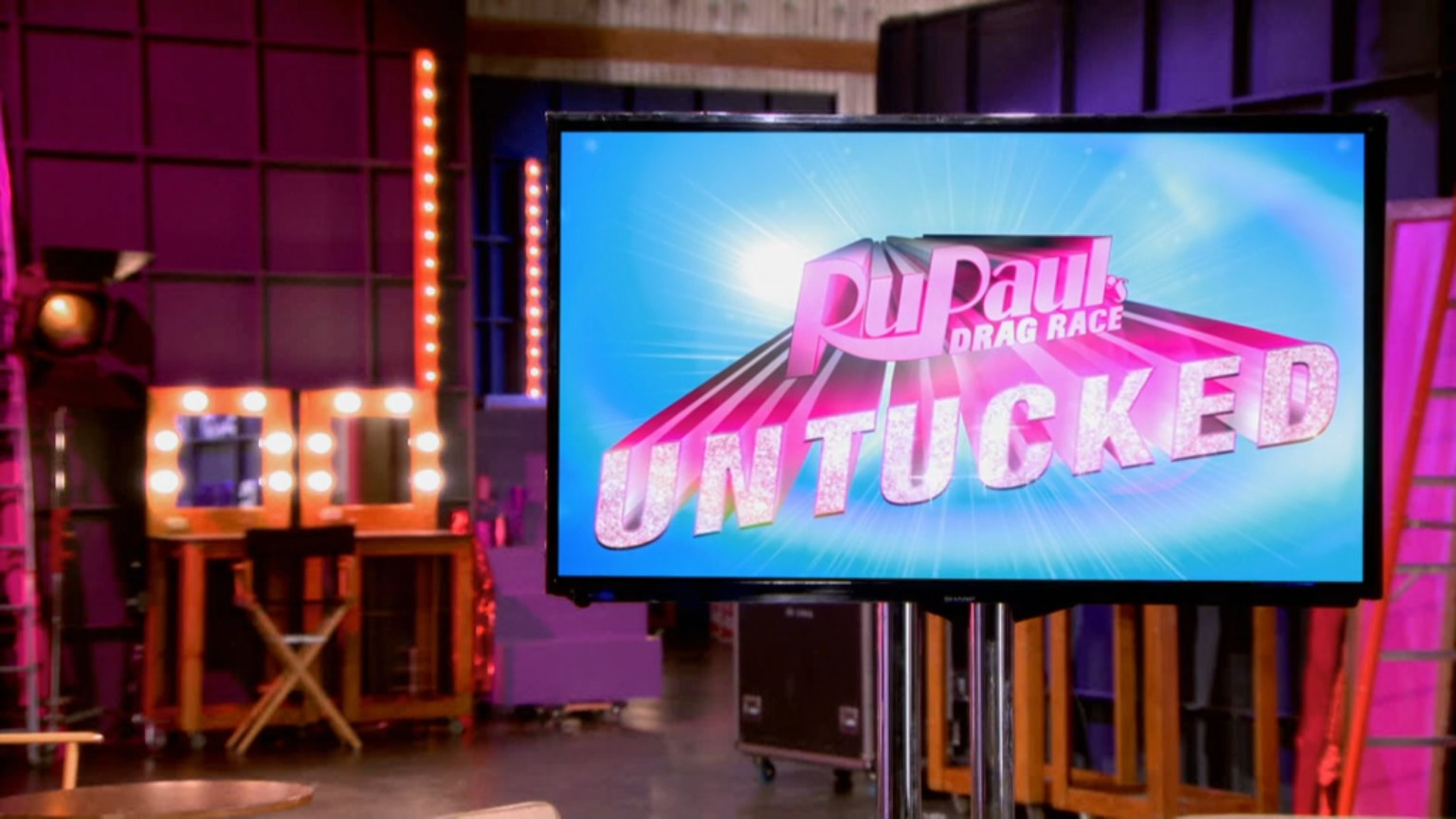 RuPaul Drag Race Untucked set. The image shows a screen displaying "RuPaul's Drag Race Untucked!" in a studio setup with vanity lights in the background
