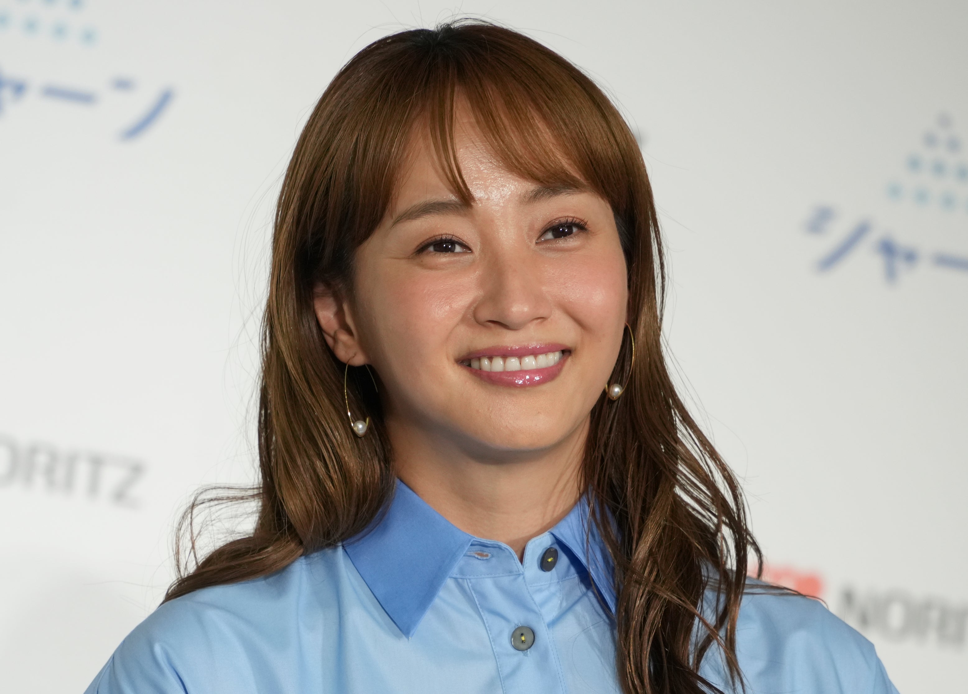 佐々木希さんが青いシャツを着て、笑顔でカメラに向かっている。背景には「ノーリツ」と書かれたロゴが見える。