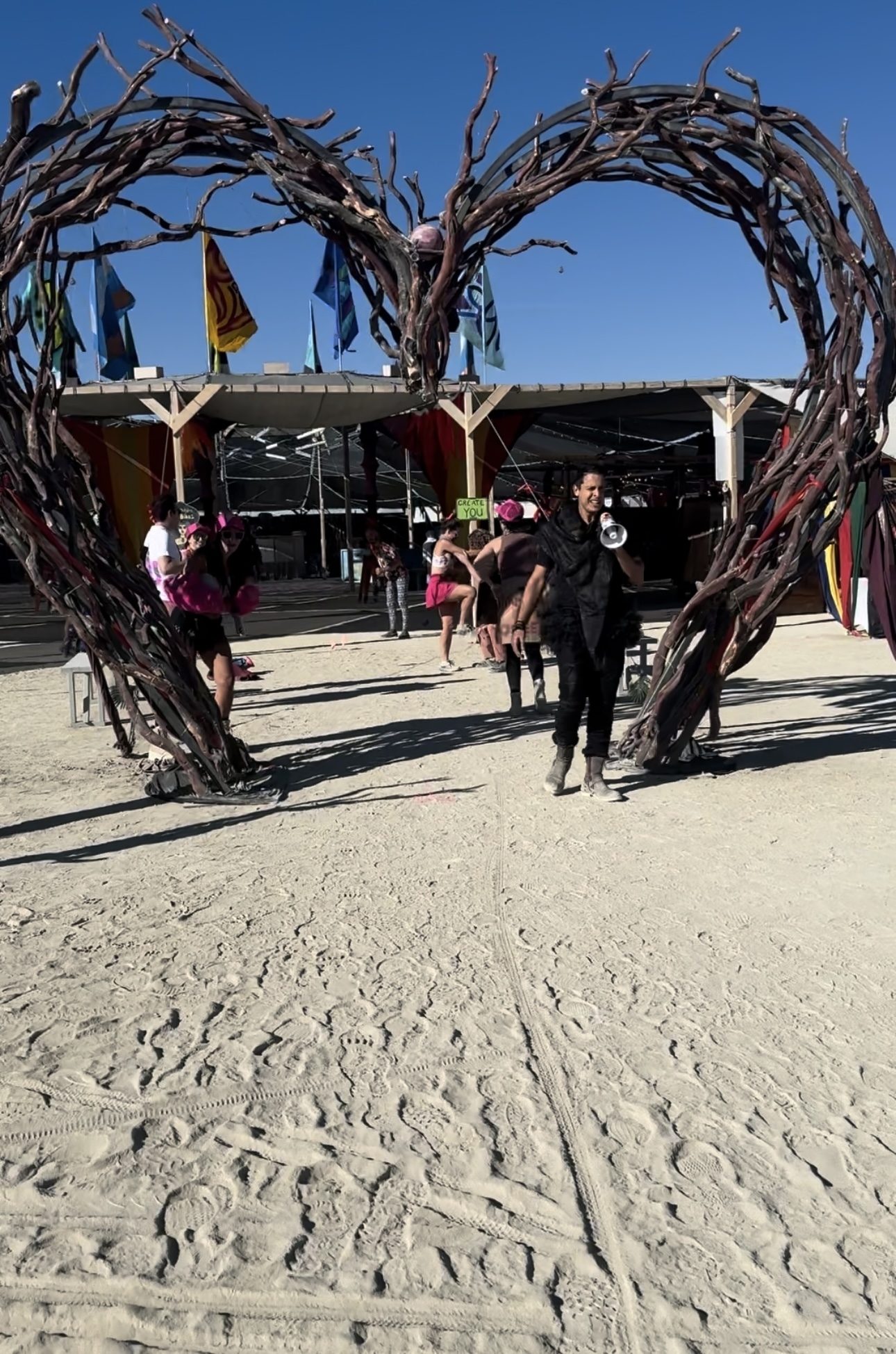 People are walking under a large heart-shaped arch made of branches at a cheering station during the Burning Man Ultramarathon 2024