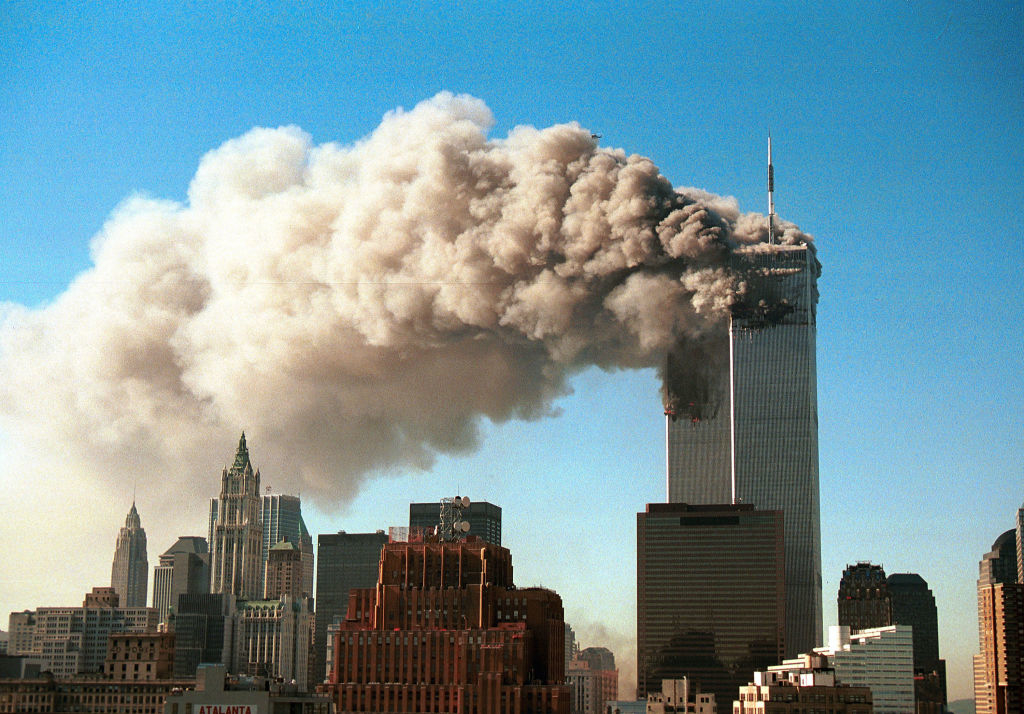 The image shows the World Trade Center towers in New York City during the 9/11 attacks, with smoke billowing from the upper floors where planes struck