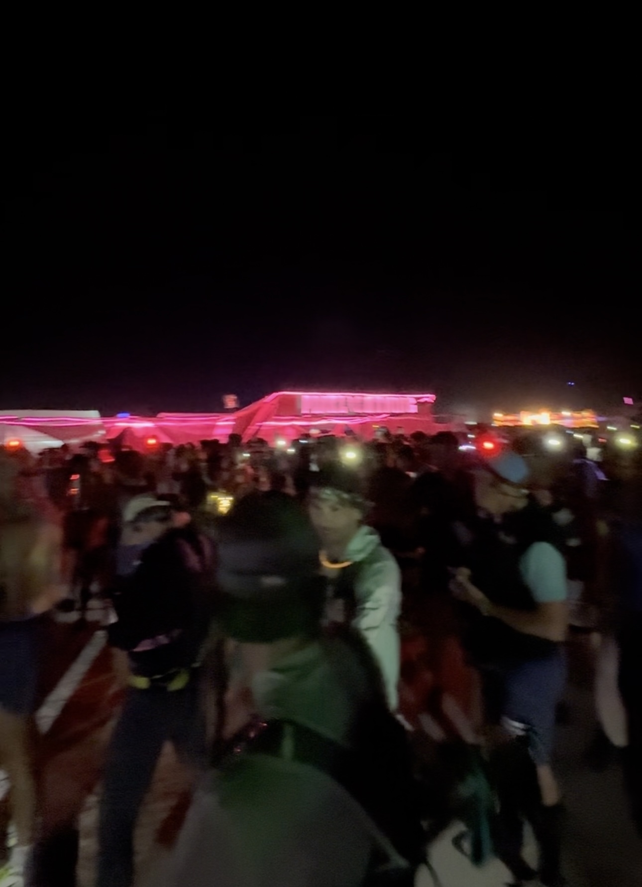 A large group of people gathered at 5am for the Burning Man Ultramarathon, with some wearing reflective headgear and safety vests. Dimly lit structures and lights are visible in the background