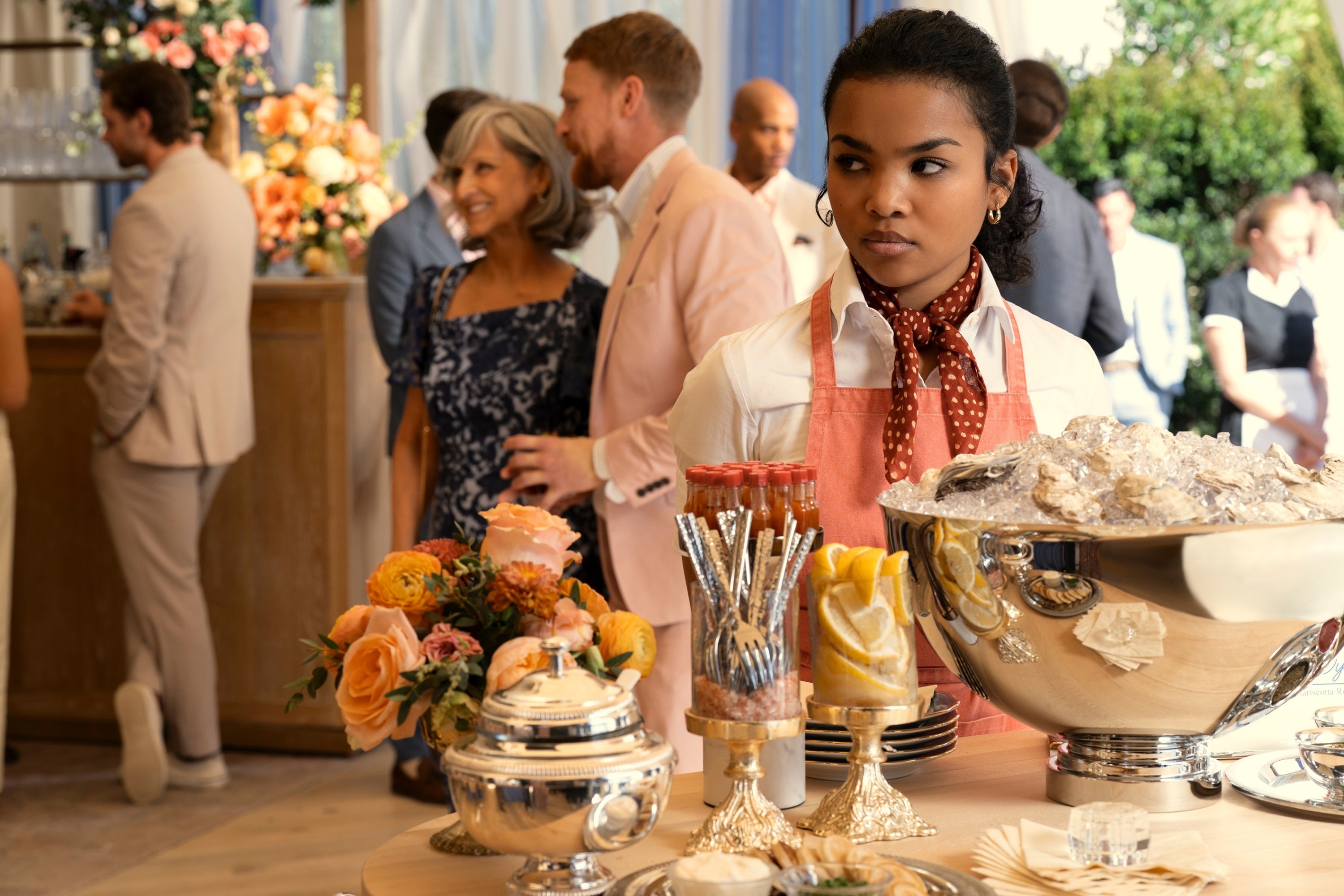Mia Isaac standing by a table of appetizers in "The Perfect Couple"