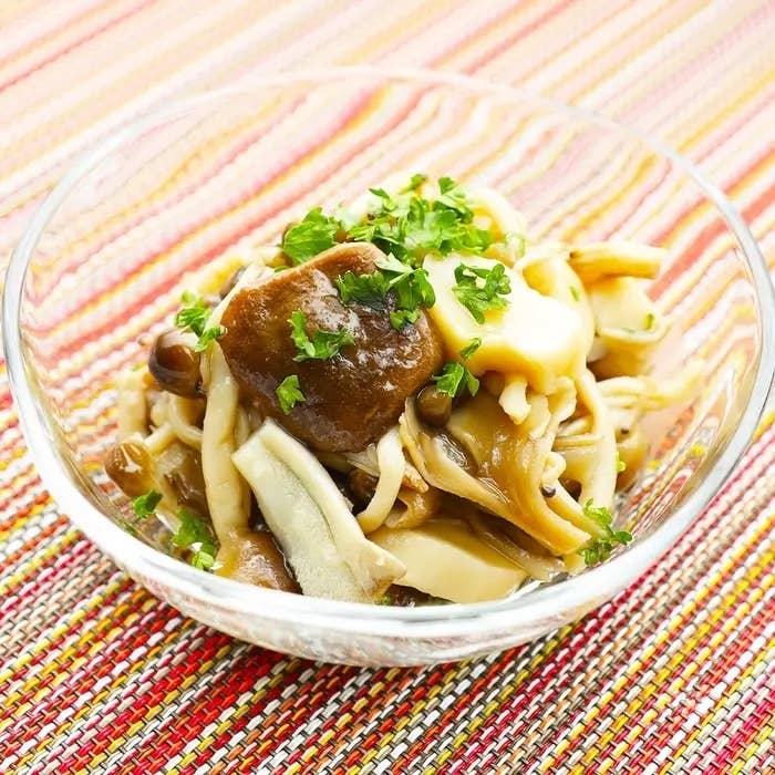 透明のガラスボウルに盛り付けられた、パセリがかかったキノコのサラダ。背景はカラフルなテーブルクロス。