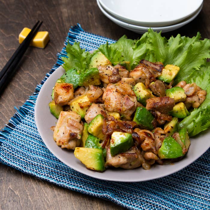 皿に盛られた鶏肉とアボカドの料理が葉野菜とともに並んでいる。人民共和国のチョップスティックと皿が背景に置かれている。