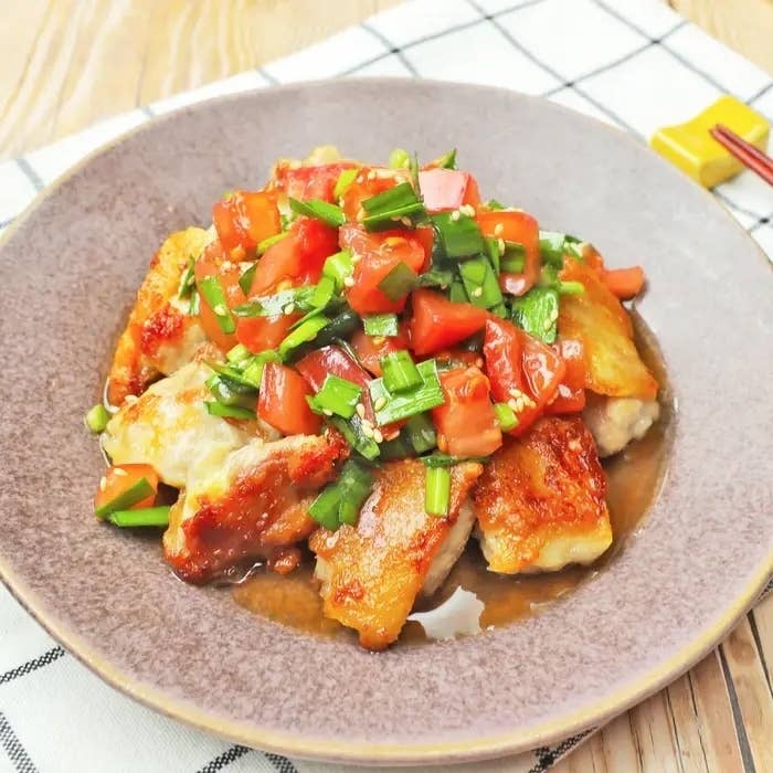 白いプレートに乗った鶏肉のトマトとネギのソース添え料理がテーブルクロスの上に置かれています。