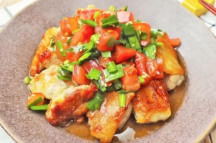 皿に盛り付けられたトマトとネギのソースがかかった焼き鶏の料理。