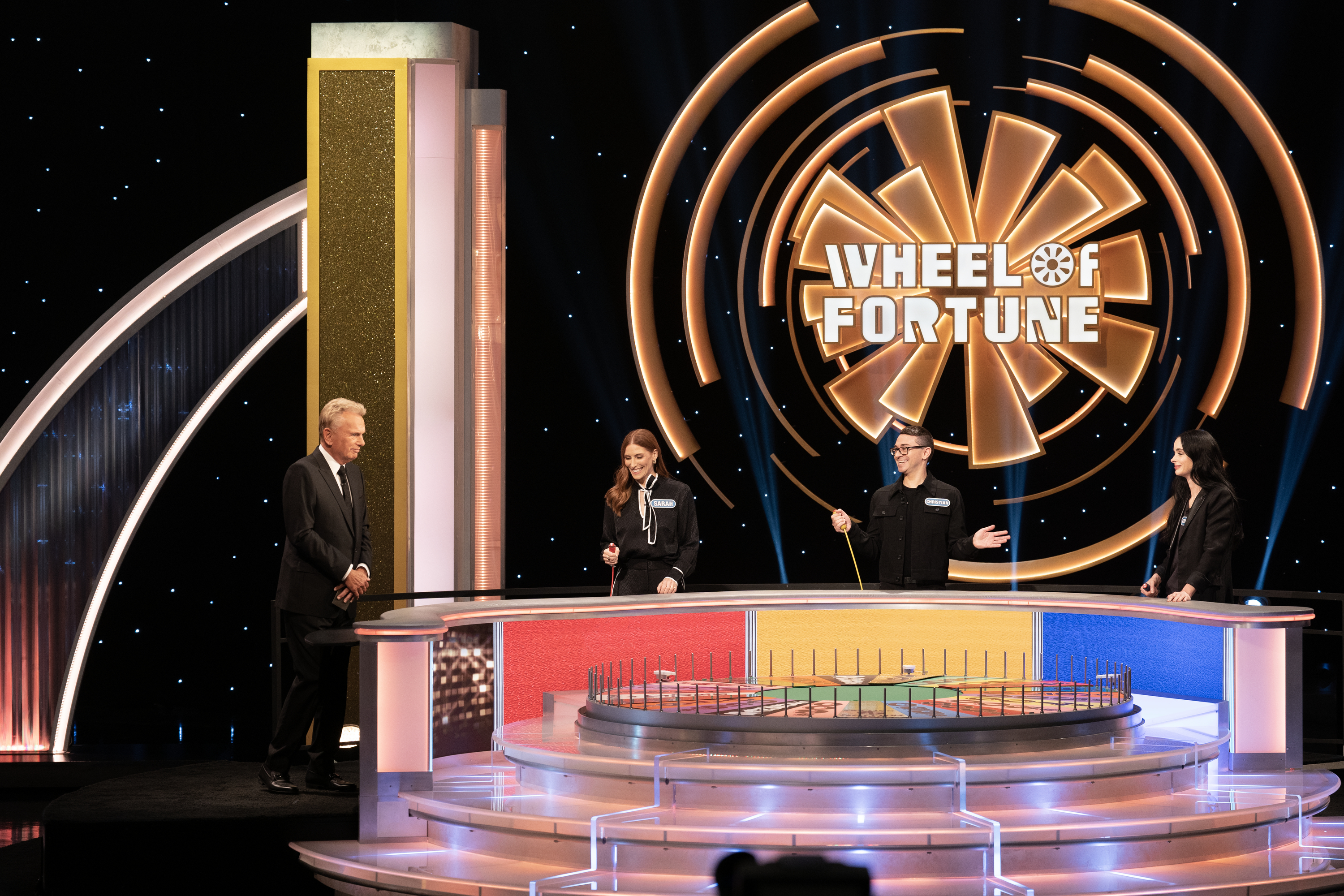 Four people on the Wheel of Fortune TV game show set