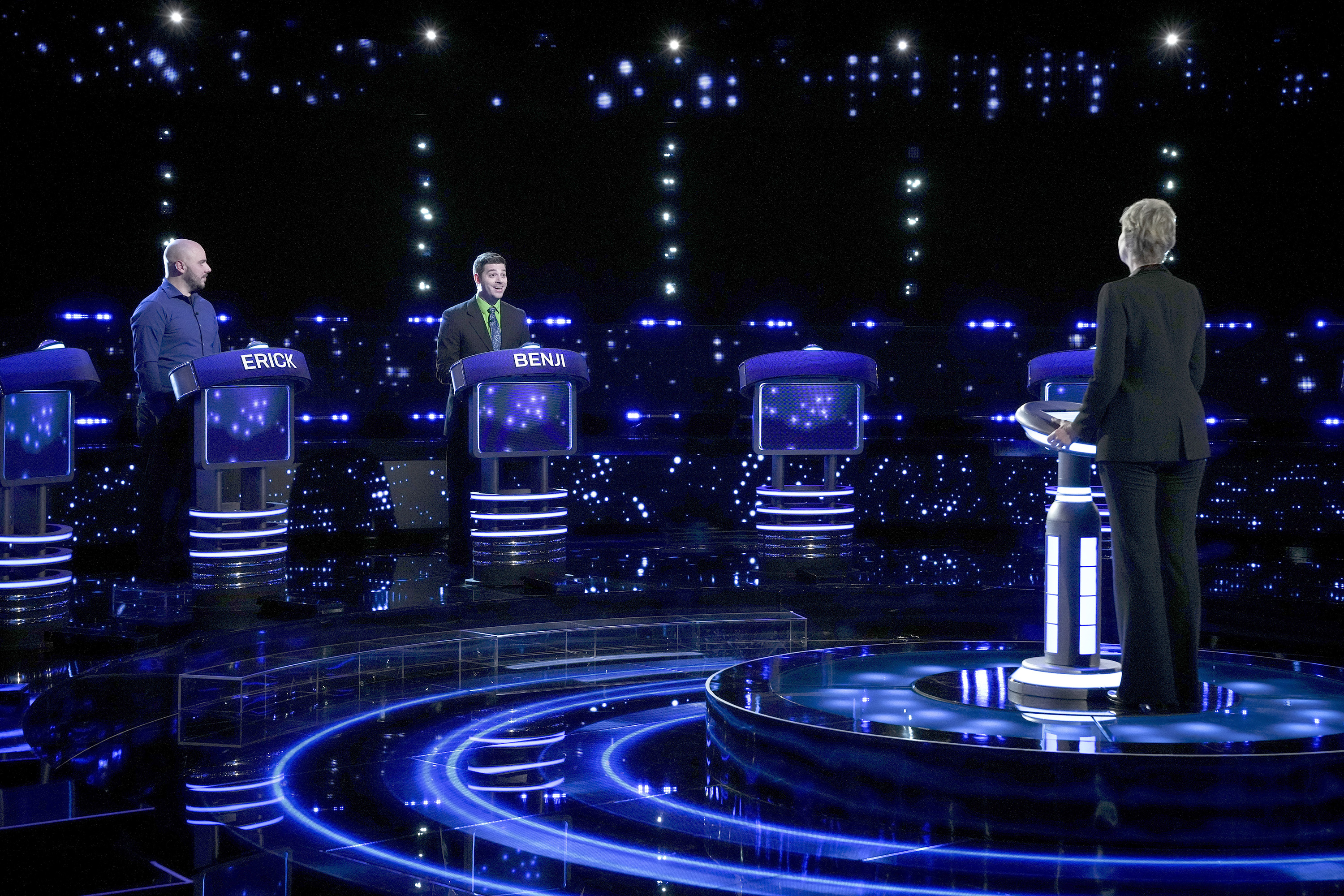 A game show set with bright, illuminated podiums and a starry backdrop