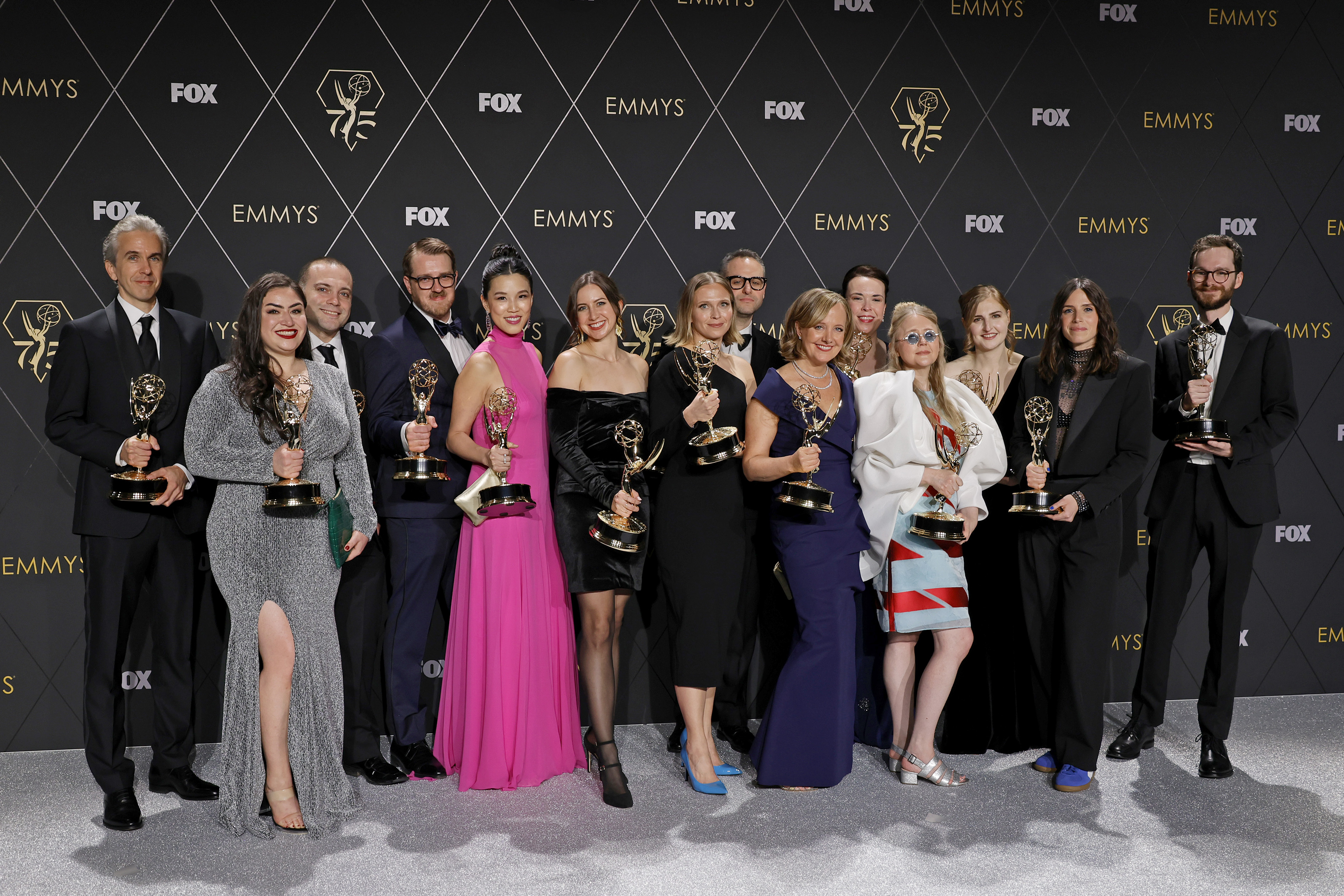 A large group of people stand on a stage holding Emmy awards, dressed in formal attire