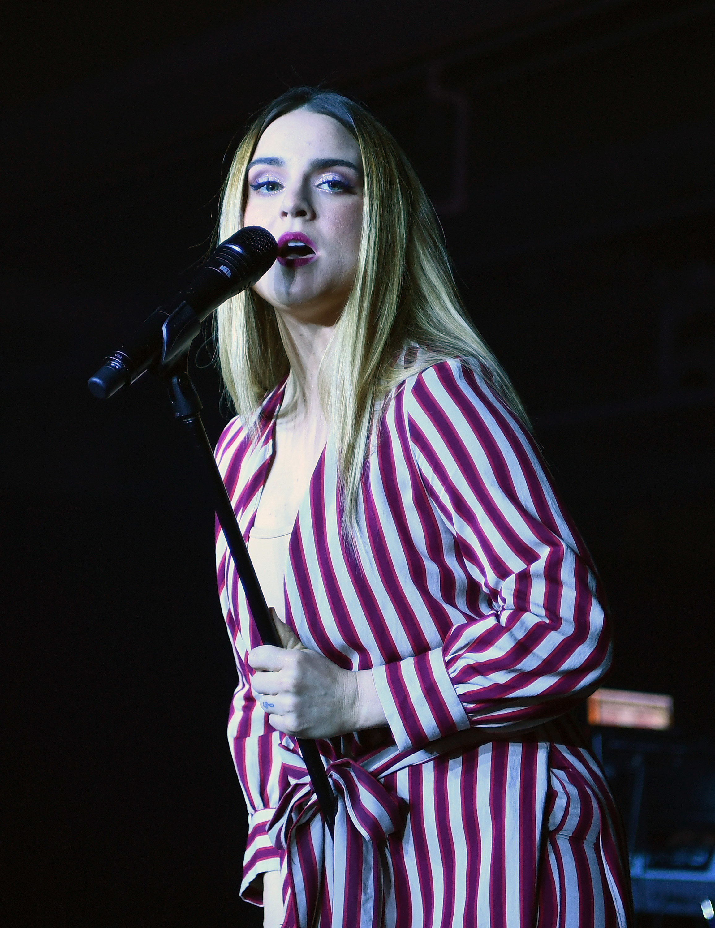JoJo on stage singing, wearing a striped, belted outfit