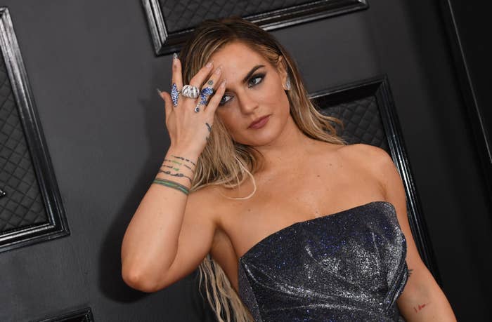 JoJo on the red carpet in a strapless metallic dress, with her hand near her face displaying multiple rings and bracelets