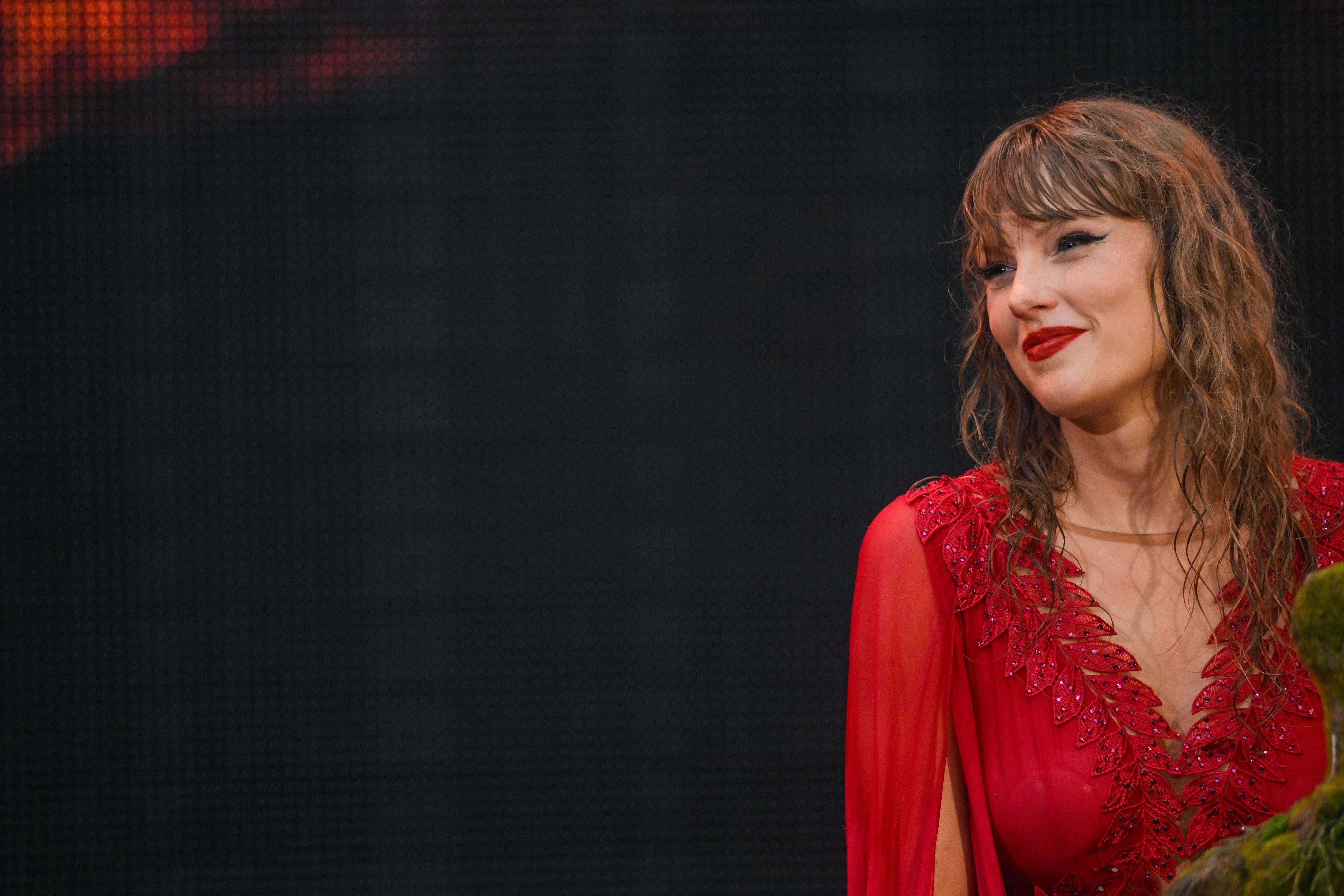 Taylor Swift in a glamorous, long dress with intricate detailing, smiling on stage